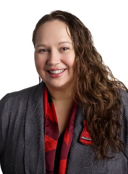 Portrait of a smiling woman with long wavy hair wearing a red shirt and grey blazer