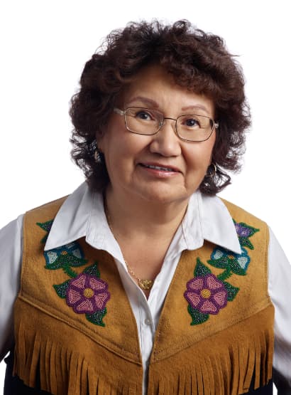 A woman with short curled hair wearing glasses, a white shirt and beaded vest