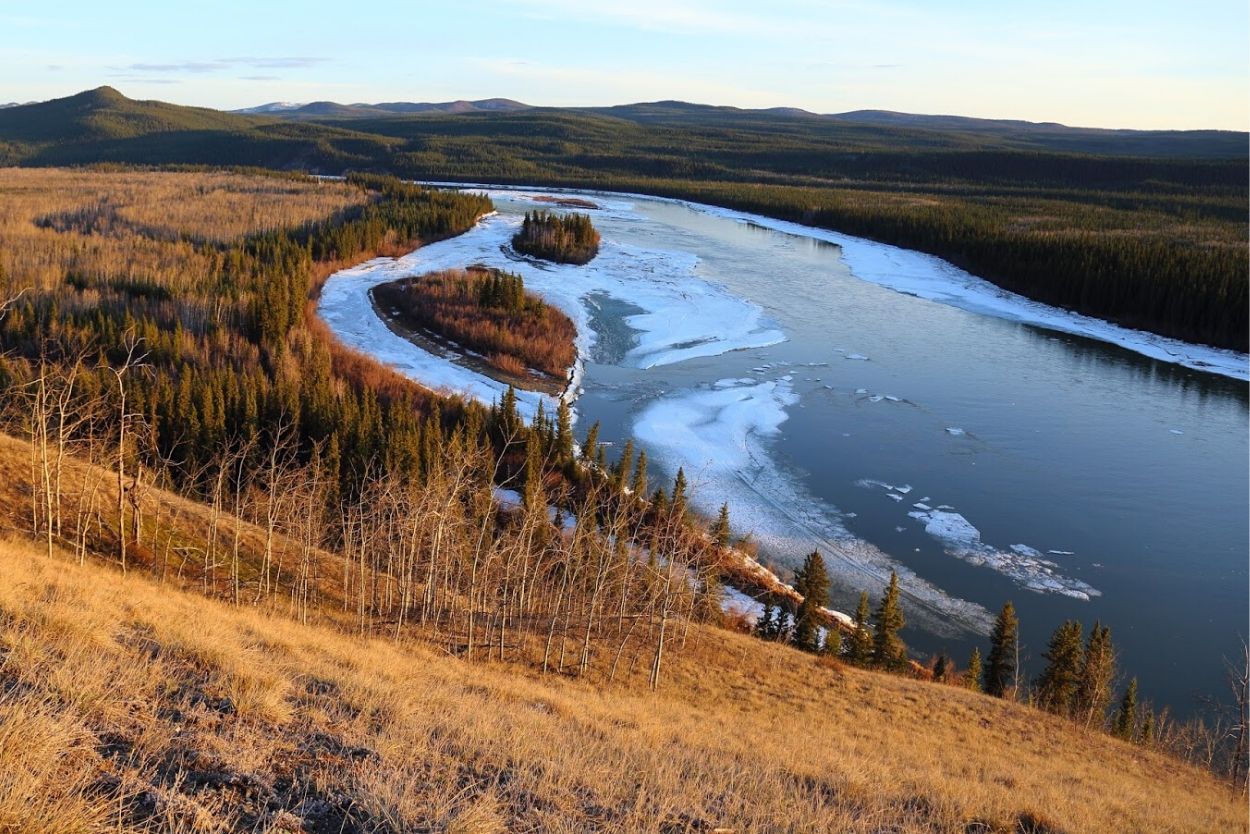 Partially frozen over river in the fall with golden grass and trees along the river banks