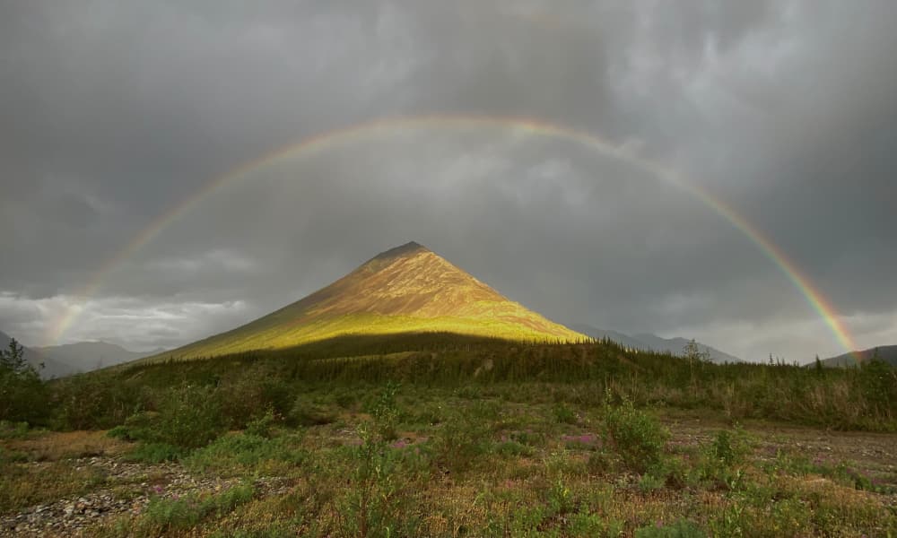 A mountain illuminated by sunlight with a full rainbow arcing over it