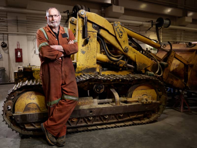 Doug McCrae posing in overalls in front of heavy equipment