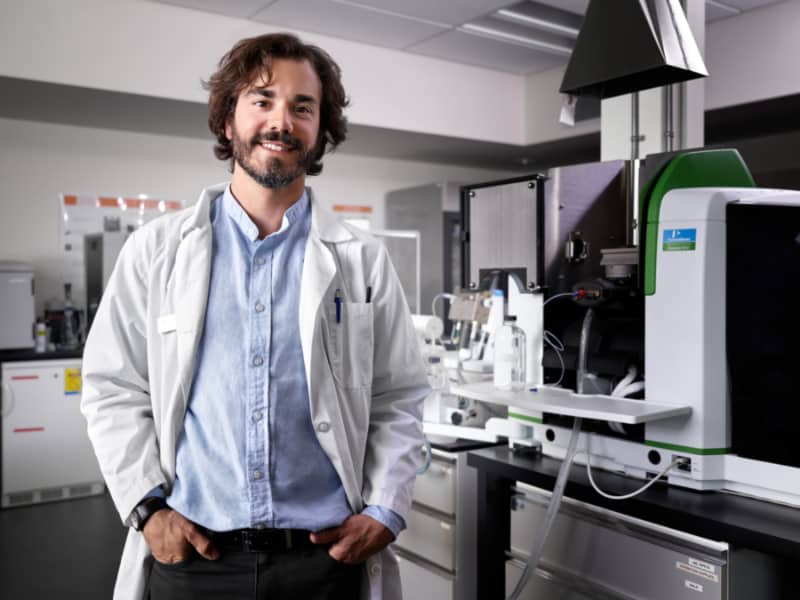 Guillaume Nielsen poses in a lab jacket in front of research lab equipment