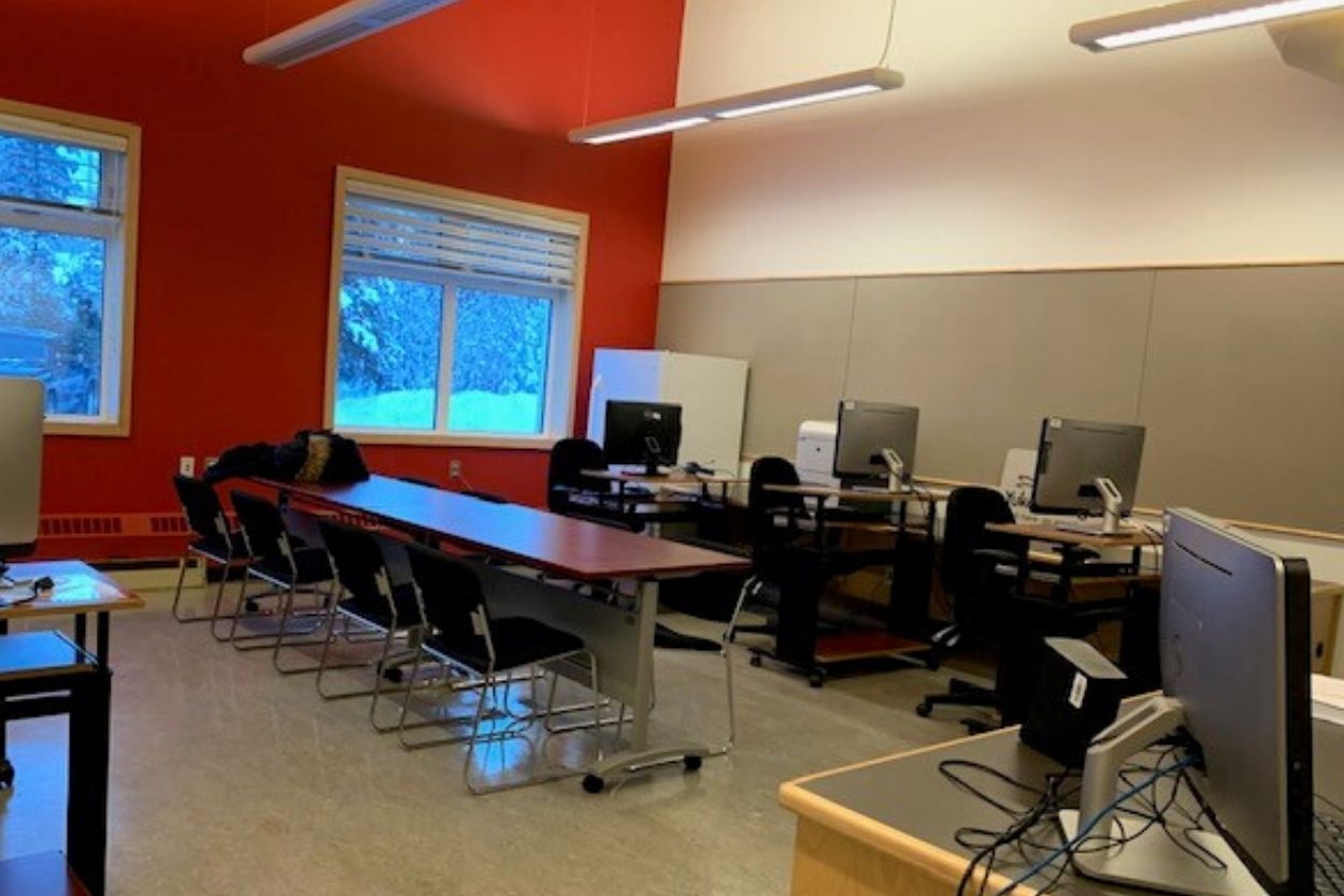 A computer lab with a high ceiling and one red wall with two windows facing out to a snowy exterior