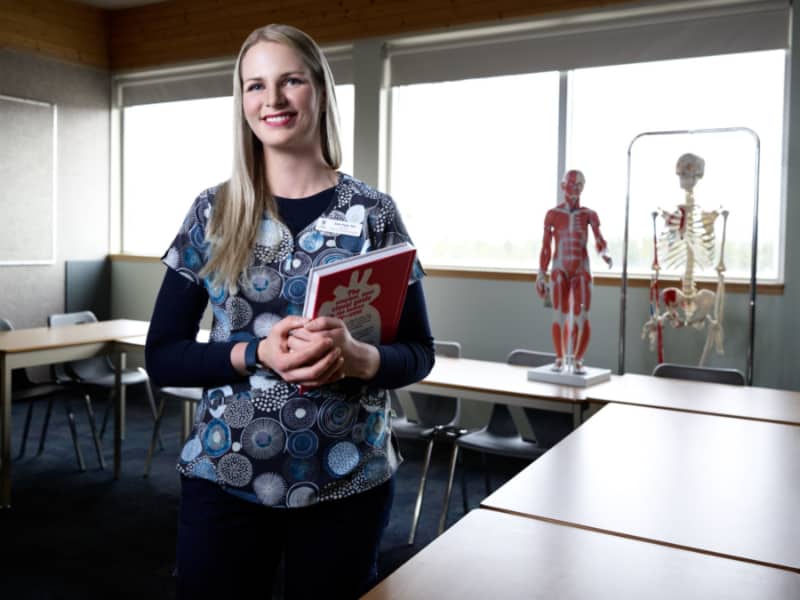 Samantha Piper poses holding a text book in a nursing classroom