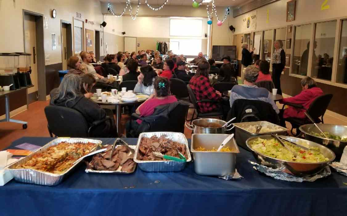 A large group of people seated at tables behind a row of dishes of prepared food