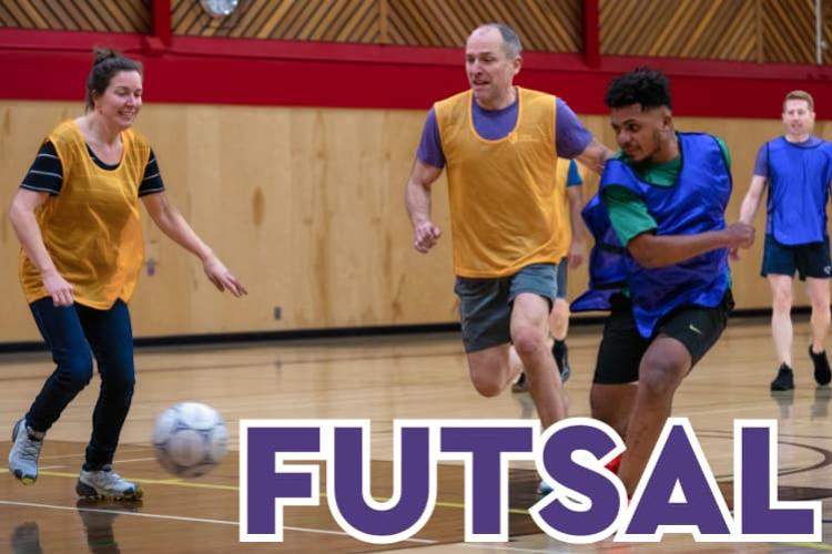Students and staff wearing blue and yellow jerseys and playing soccer in an indoor gym