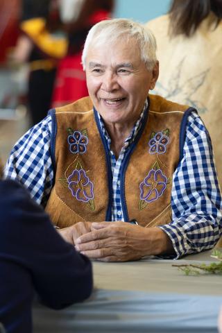 Stanley Njootli seated at a table, smiling, wearing a beaded vest