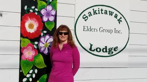 Woman stands in front of building with flowers and logo