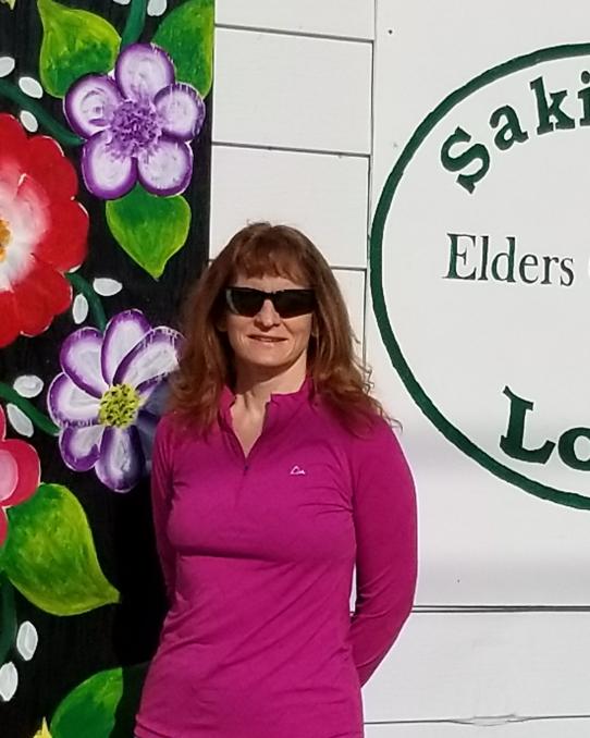 Woman stands in front of building with flowers and logo